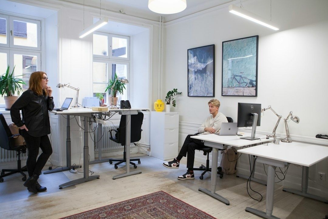 Helles Büro mit zwei Personen an höhenverstellbaren Schreibtischen und Monitoren